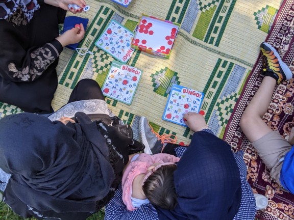 Students play alphabet bingo on a blanket at a park to practice English