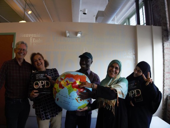 A class of students gathers after an English course, with a globe. Smiles.