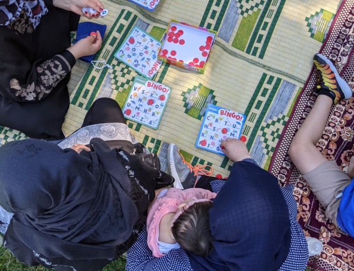 Students play alphabet bingo on a blanket at a park to practice English