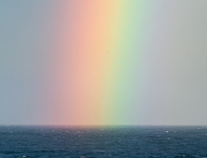 Blurred Rainbow in the sky over a sea Photo by Ben Mack